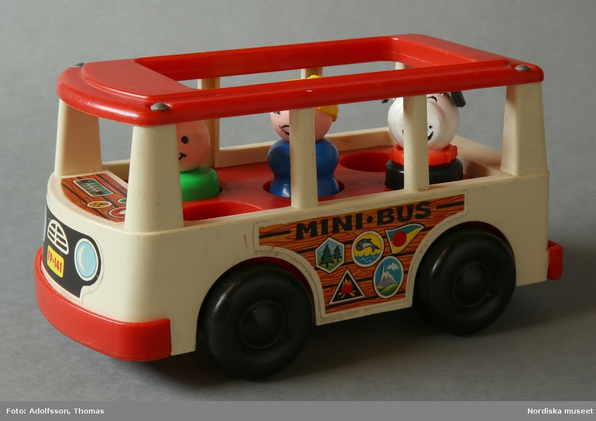 Minibuss, leksak av hårdplast tillverkad av Fisher Price, röd och vit, med 4 rörliga hjul. Metalldelar och masonitbotten. Inuti bussen finns fem hål för tillhörande figurer. Tre figurer placerade, en kvinna, en man och en hund.