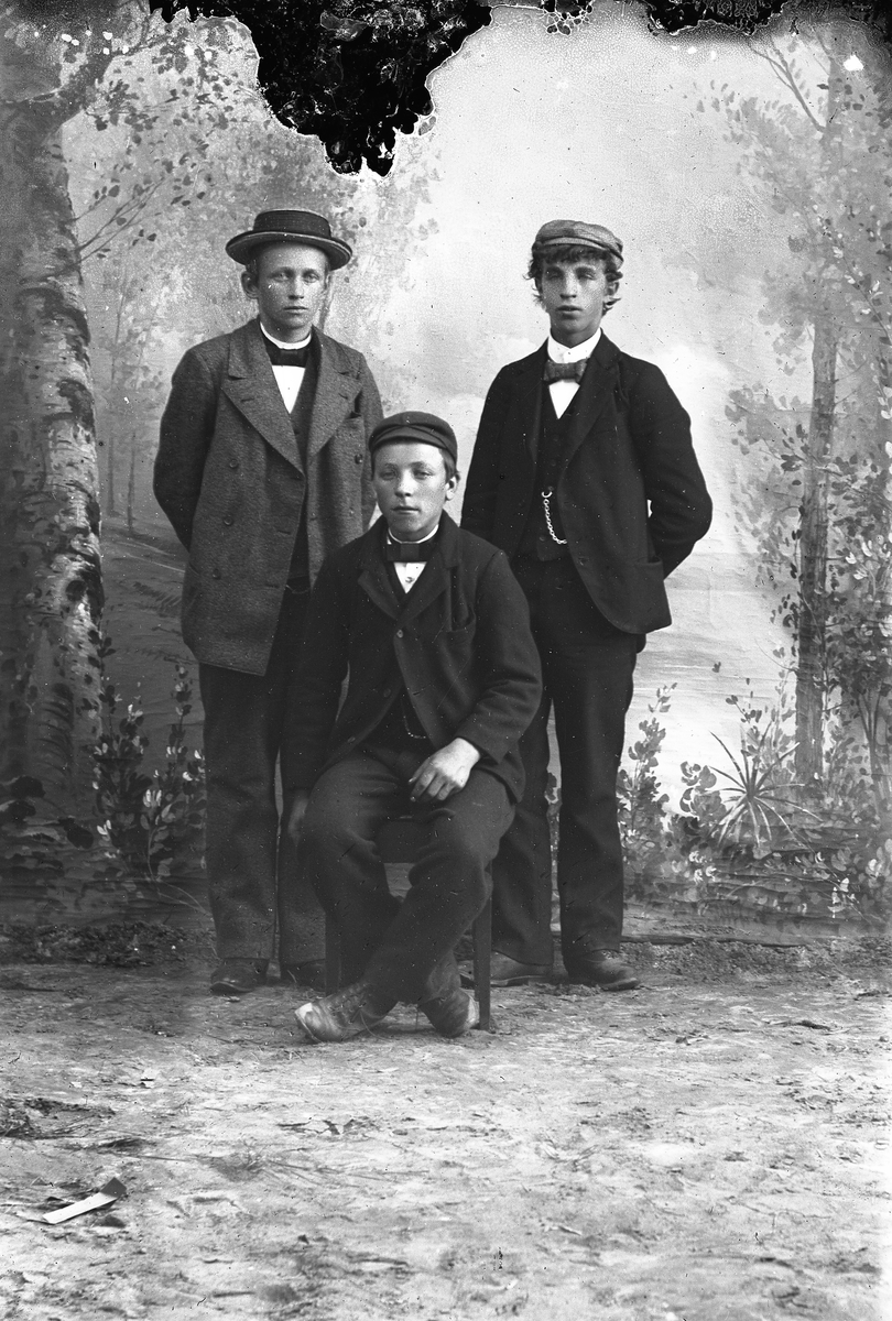 Tre unge menn/gutter, to står og én sitter.