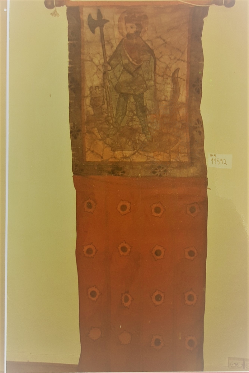 Øvre del: Olav Haraldsson med krone, kappe og øks, som står på en "underligger" formet som en drage med menneskeansikt. Nedre del: påsydde blomster