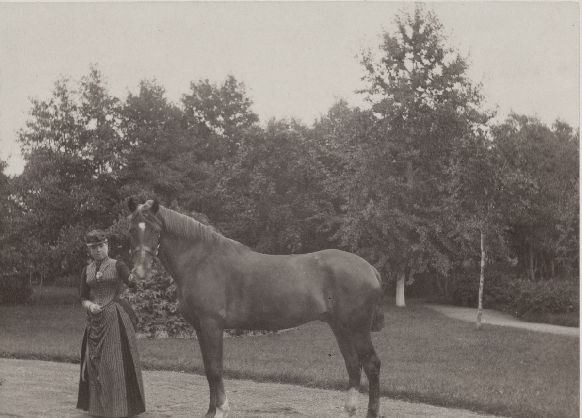 Antonie Rettig, stående tillsammans med häst i en trädgård, sannolikt vid Villa Rettig, Gävle.