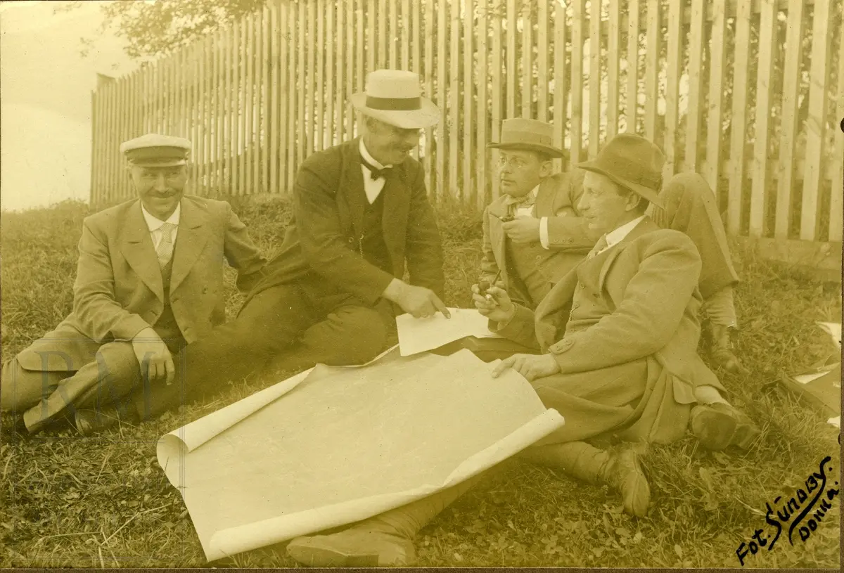 Fire menn sitter med en tegning eller kart mellom seg