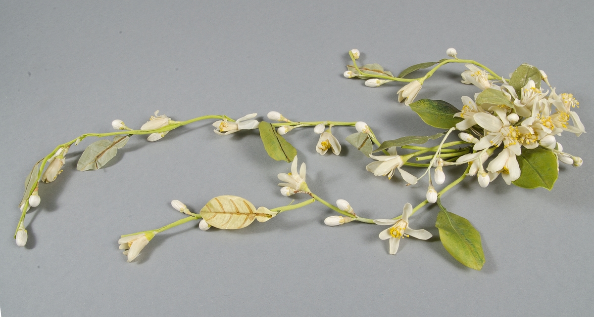 Girland längd ca 50 cm. Krans diameter ca 16 cm. Vita och orange blommor och gröna blad av vitt skinn och vaxat tyg.

