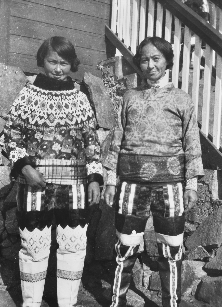 To grønlandske kvinner i sine folkedrakter poserer foran et hus.