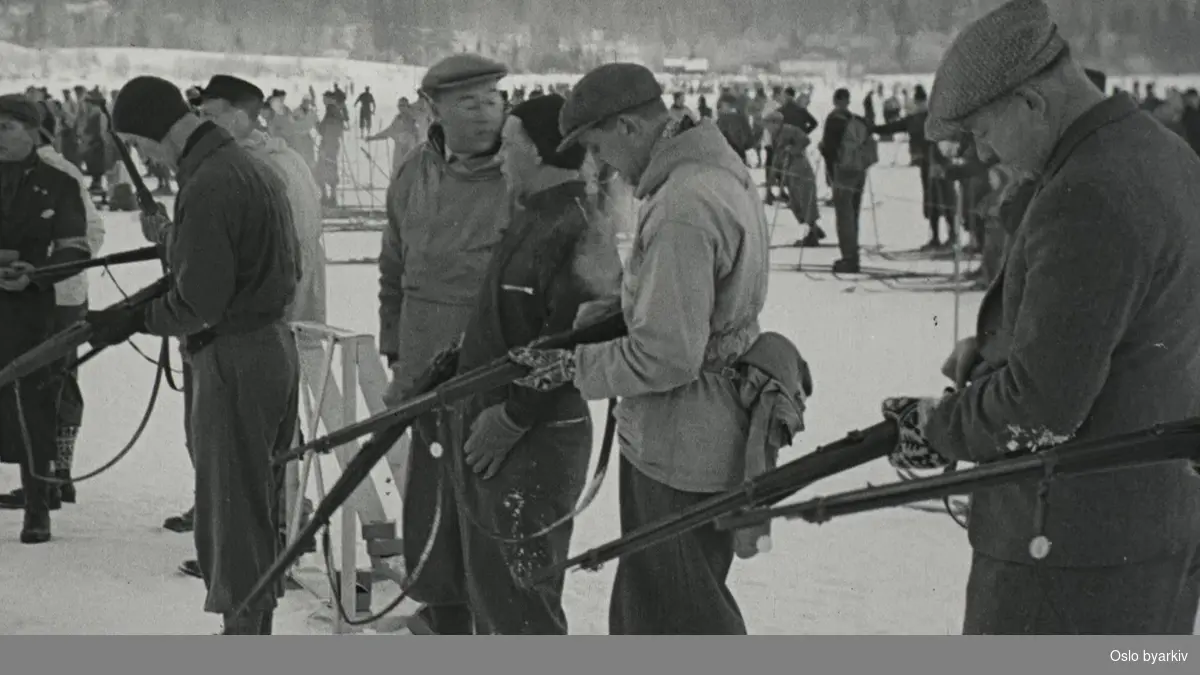 Publikum og skyttere på Bogstadvannet, trolig 7. januar 1940. Det gis intruksjoner i bruk av gevær, funksjonærer utdeler ammunisjon, det skytes på blink, og resultatet undersøkes.