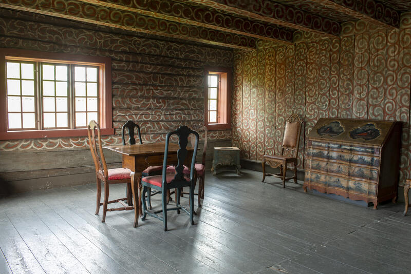 Interiør fra Bolstadbygningen viser en stolgruppe og en kiste i et rom med dekormalte tømmervegger. (Foto/Photo)