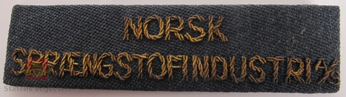 Håndsydd jakkemerke i blått, med teksten NORSK SPRÆNGSTOFINDUSTRI A/S brodert med gullfarget tråd.