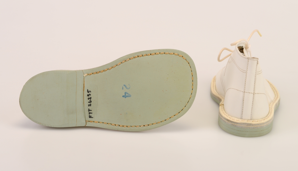 Et par barnesko i størrelse 24 i skoeske med silkepapir. Skoene er i hvitt skinn med såler av lyst grått kunstlær. De er randsydde. I front er det 3 par hull med maljer for snøring. Under snøringen er det en enkel tunge av hvitt skinn. Skoene har hvite, runde skolisser. Det er sømdekor på skoene.  Skoene ligger i en skoeske av papp som er stiftet sammen. På den ene kortsiden er det trykt på fabrikkens navn, varemerke og logo samt artikkelnummer og størrelse. Logoen er en sirkel med en Nord-pil igjennom. Logo og tekst er i rødt med påstemplet artikkelnummer og størrelse i svart. Skoene er ikke brukt.