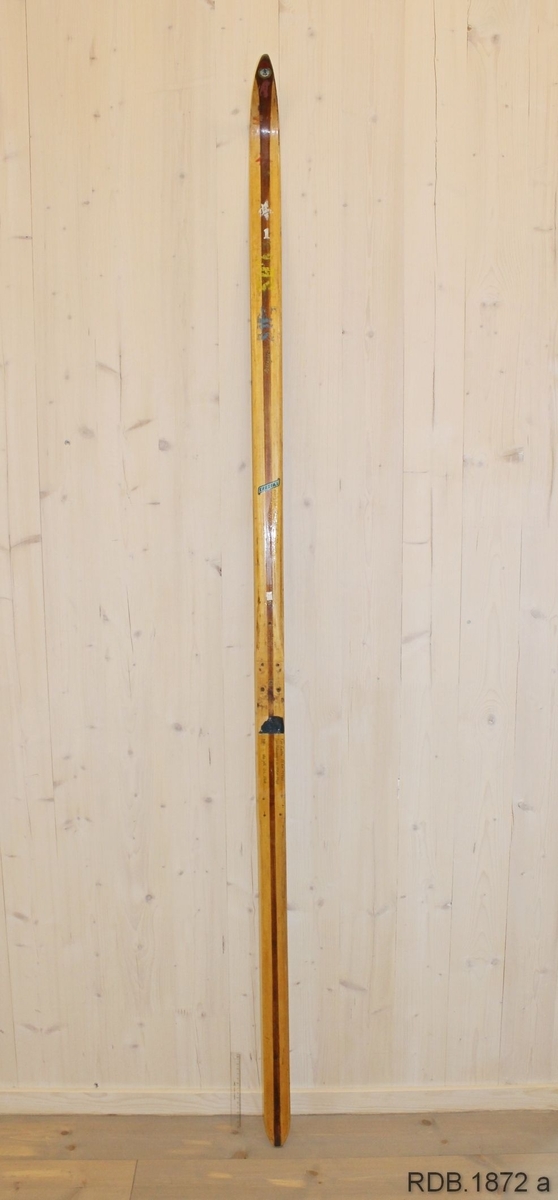 Avsmalende jevnbred ski med liten bue. Bøy uten tupp. Tilspisset brettende.
Dekorert med ei brun stripe på trehvit bunn.

Stempel fra 1960-sesongen på skiet.