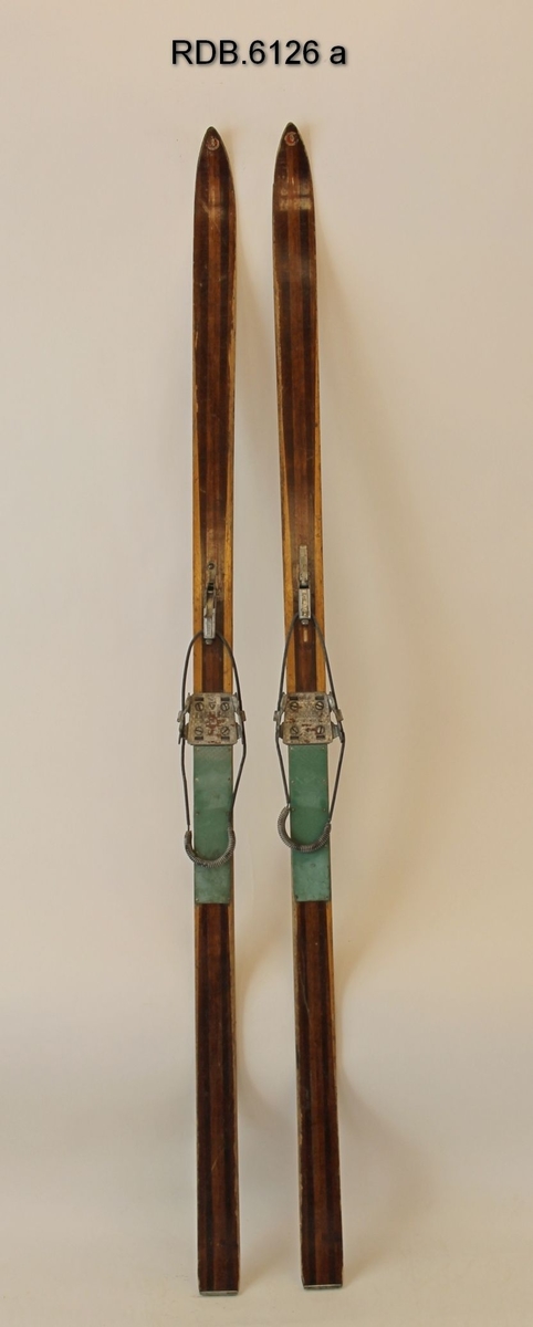 Et par brune turski med trekvite kanter og stålkanter under og bak. Splitkein-merke på skituppen. Påmontert Gresvig kandaharbindinger og grønne, faststiftede fotplater.
