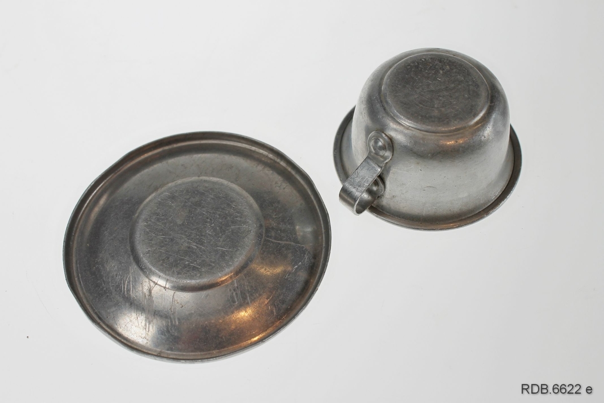 Dukke-koppesett i blikk som består av to kopper, to tefat og to asjetter. Koppene har påklinket hank.