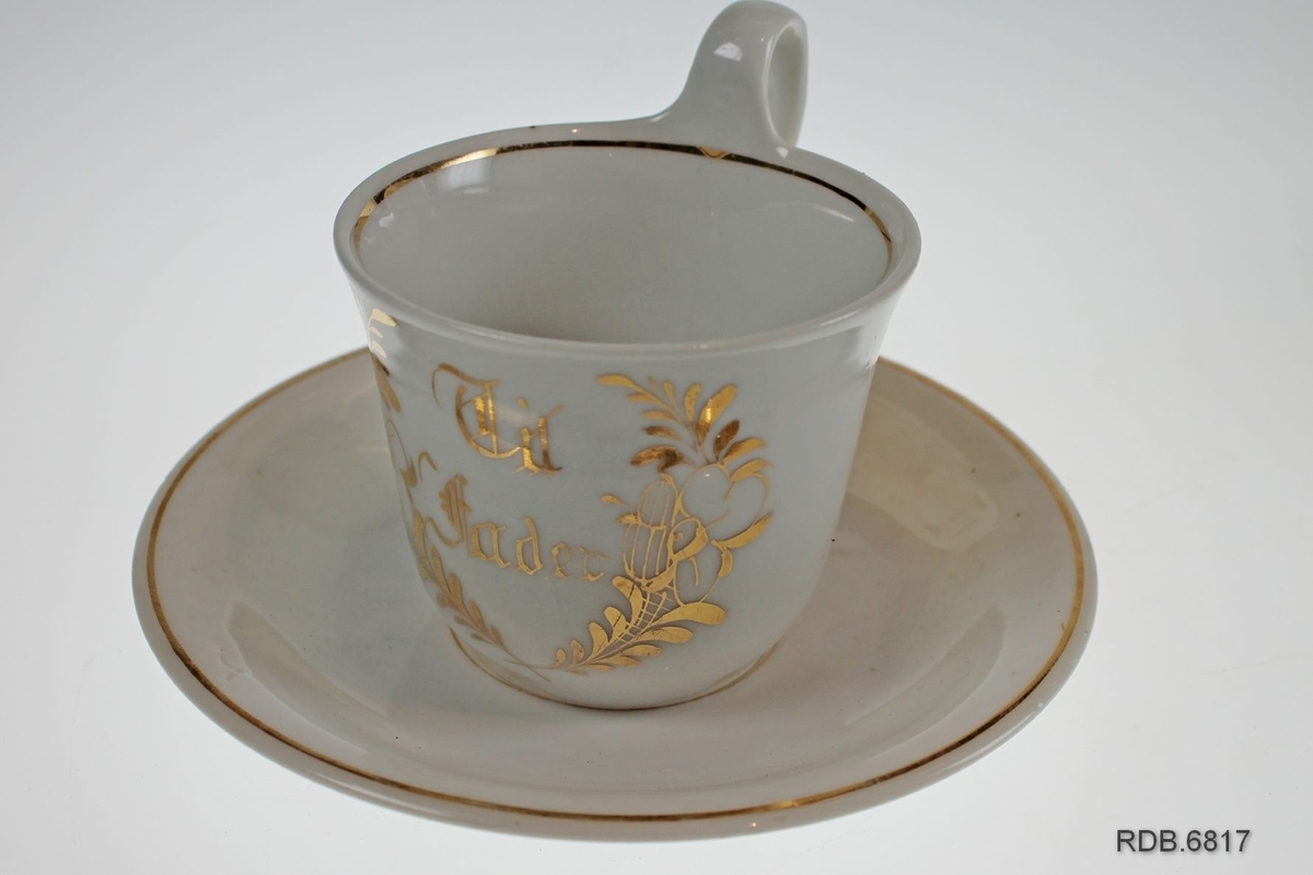 Hvit kaffekopp med gulldekor i form av blomster og påskrift "Til Fader". Gullkant øverst. Enkel skål med gullrand i bunnen og gullkant.