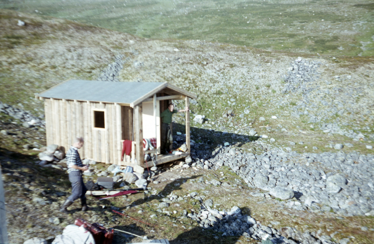 Tre menn foran ei fiskebu ved Cavajavrre i Finnmark. Nor-Wings hadde mange taxioppdrag med turister og utstyr til fiskevann. I 1967 bygde de denne enkle bua som Fylkesmannen krevde revet allerede året etter.