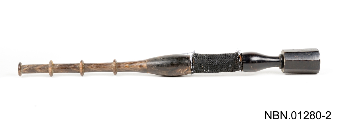Munnstykke av pipe. 
En metall munn mangler i den enden av tre munnstykket.
En del av tre kroppen er dekket av svar tråd/stoff.