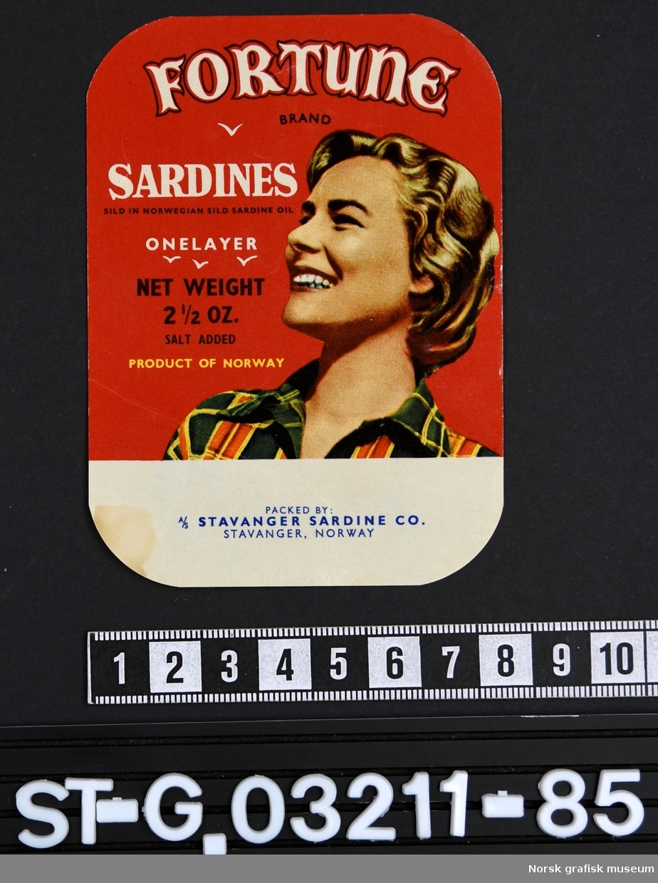 Etikett med rød bakgrunnsfarge og illustrasjon av en smilende blond kvinne i rutet skjorte.

"Sardines sild in Norwegian sild sardine oil"