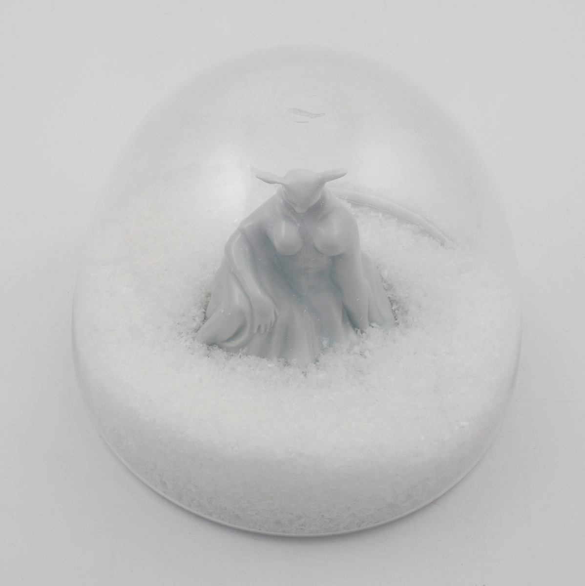 Hvit porselensfigur med rådyrhode og menneskekropp, plassert i omsluttende glasskuppel med kunstige snøfnugg.
