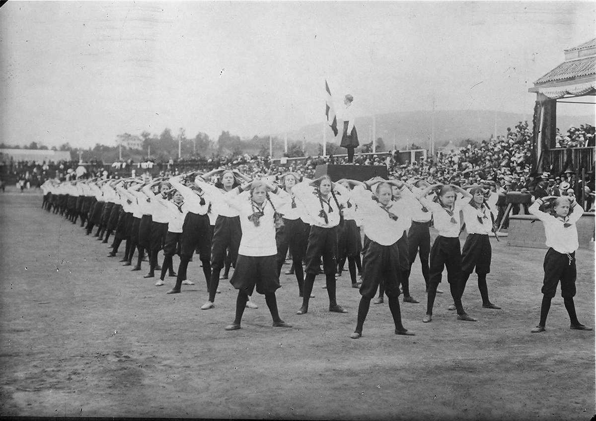 Oppvising av unge jenter på arena, tilskuere på tribunen. Fotografert 1924.