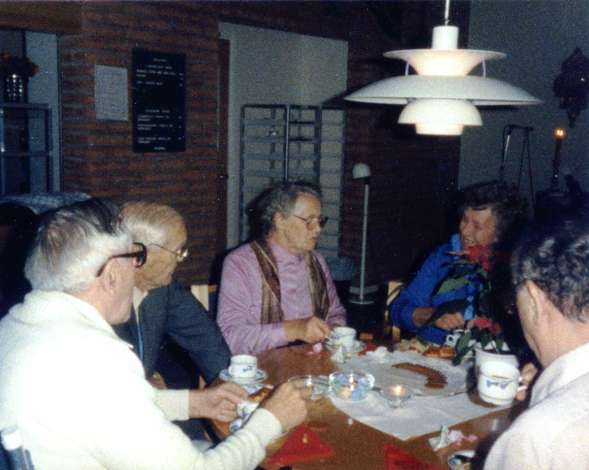 Äldre boende som dricker kaffe i Brattåsgårdens matsal (Streteredsvägen 5) omkring 1986 - 1990. Sittandes från vänster är 1. (fd postiljon) Knut Jerkfelt, 2. Valle Svensson, 3. Elin Jansson, 4. politiker Stina Svensson och 5. Okänd man. I taket hänger en vit PH-lampa (som formgavs 1924 av den danske arkitekten Poul Henningsen).