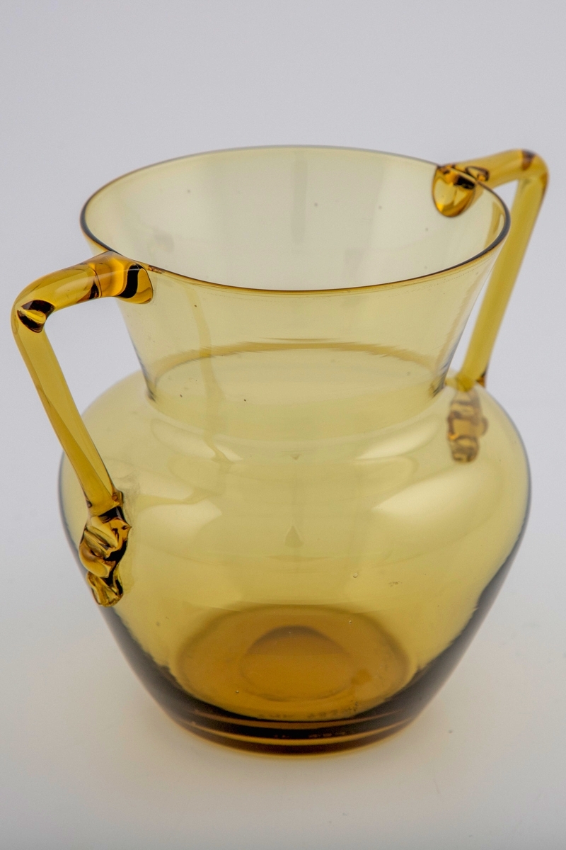 Amforaformet vase i gjennomskinnelig gulgrønt glass. Kuleformet korpus og konisk hals, to bøyde glasstaver fungerer som påsatte håndtak. Puntemerket delvis bortslipt