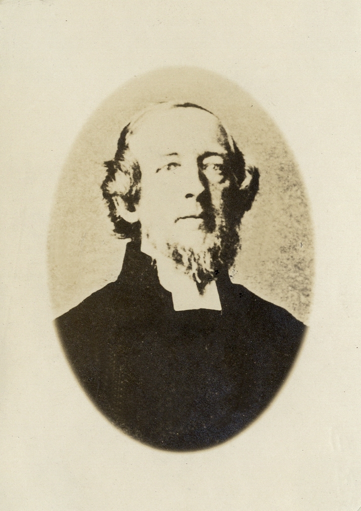 Foto av en man med pipskägg, klädd i prästrock och prästkrage.
Bröstbild, halvprofil. Ateljéfoto.

Kopia av äldre foto.