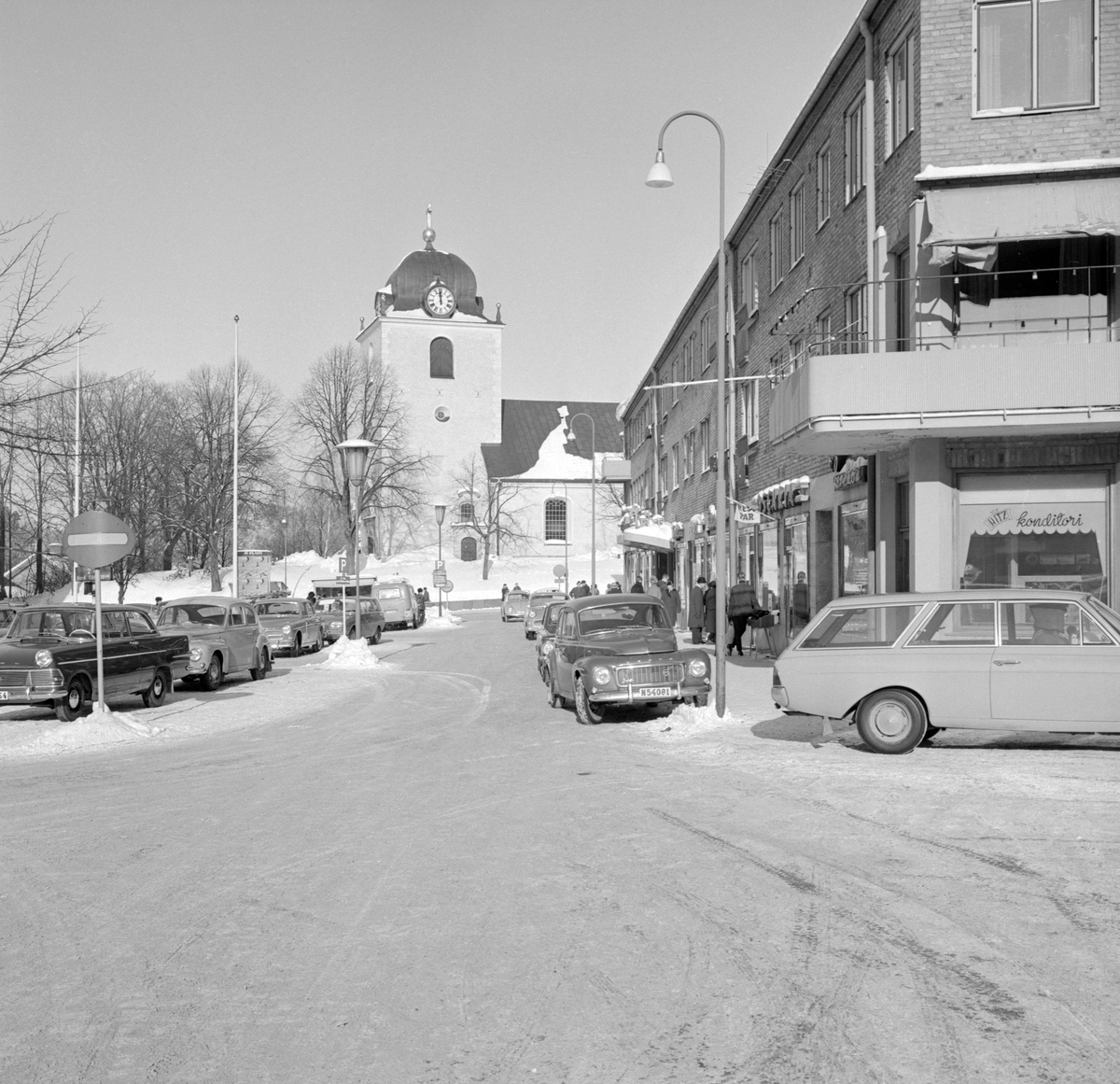 Vy över Stora torget i Mjölby vårvintern 1966 med en kavalkad av tidens bilmodeller.