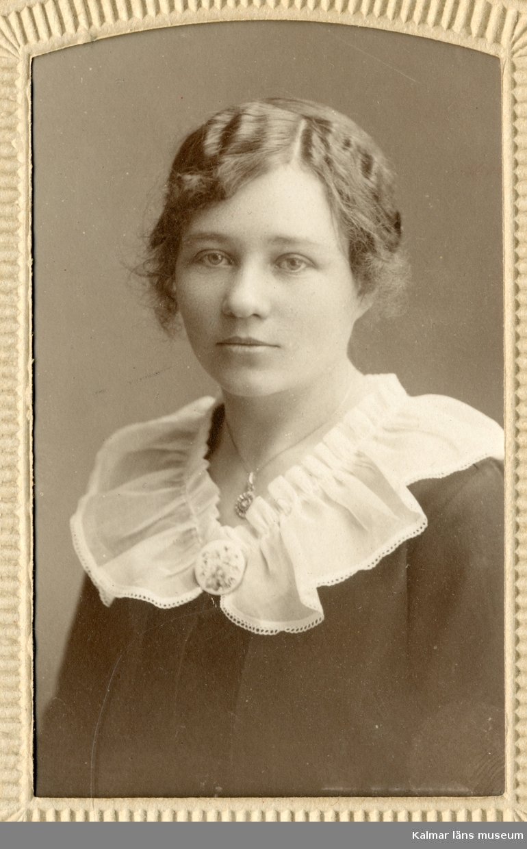 Porträtt av Esther Sivgård klädd i mörk blus eller klänning med vit krage.