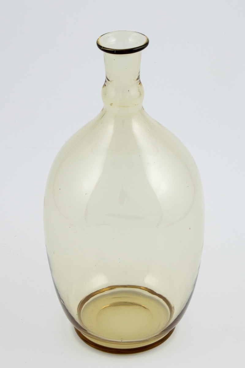 Vinkaraffelen er utført i olivengrønnfarget gjennomskinnelig glass. Korpus er ovalformet med lav hals.