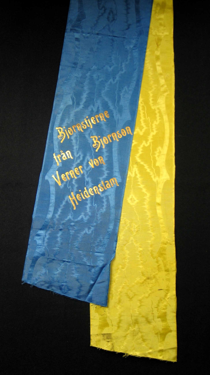 Begravelsessløyfe i blå og gul mønstret silke.