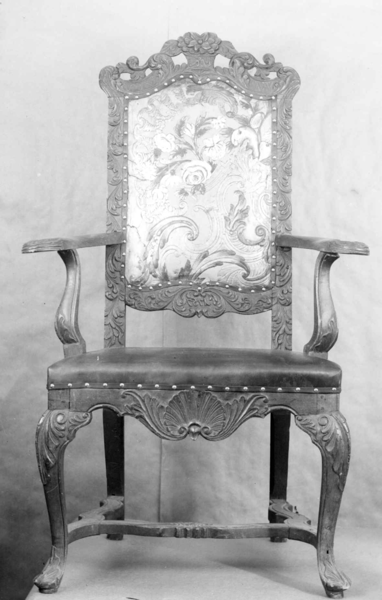 Armstol i umalt bøk og bjørk med skinntrukket rygg og sete. Ryggen har gyldenlær. Utskjæringer på rygg, armlener, sarg og bein. På ryggen er det skrevet NK og 1757. 