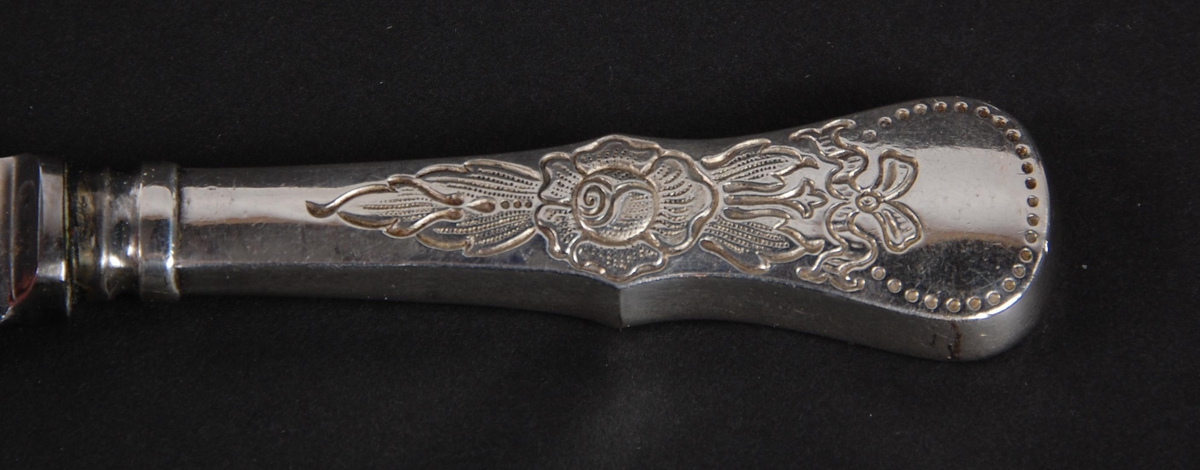Kniven har skaft av 20-gram sølv, mønsteret er Rose. Skaftet er av rustfritt metall. Stempelet har et navn (mellom TRADE MARK som er vanskelig å lese.