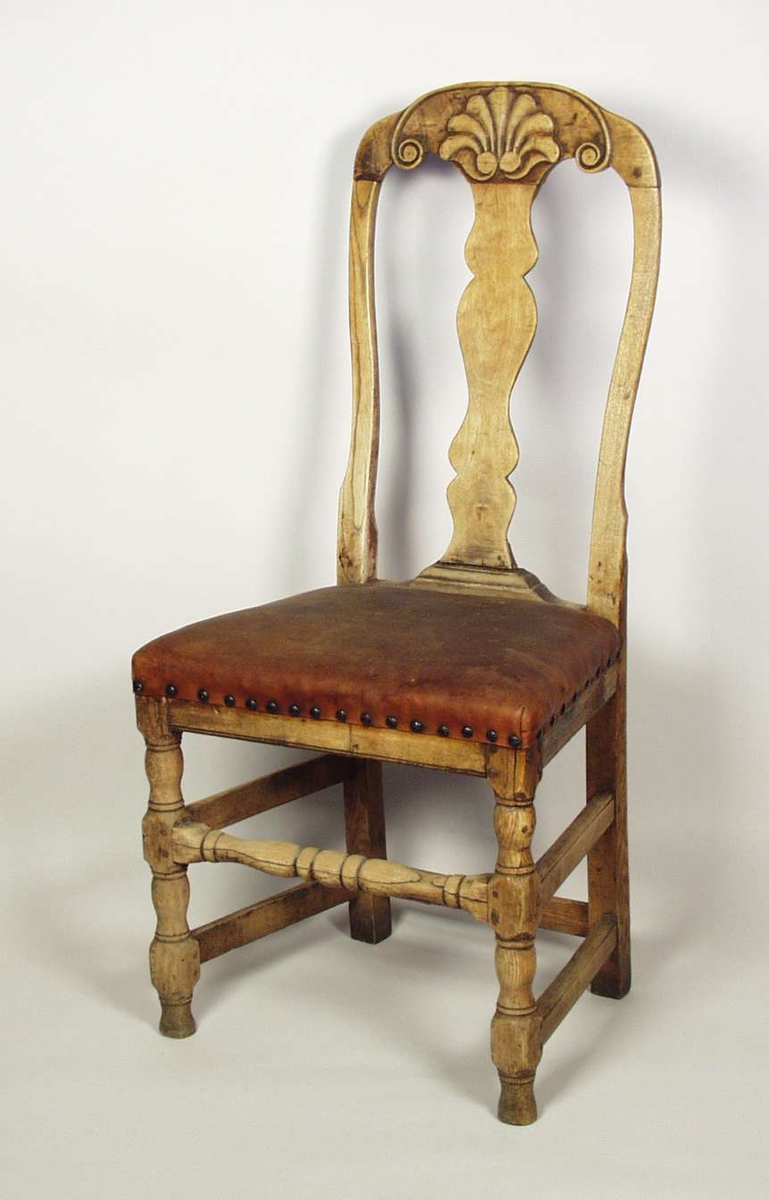 Høyrygget stol med polstring dekket med lær. Stolen er lutet. Stolen har dreiete forben og dreiet bindingsspross foran. Stolen har skjelldekor i toppstykket.