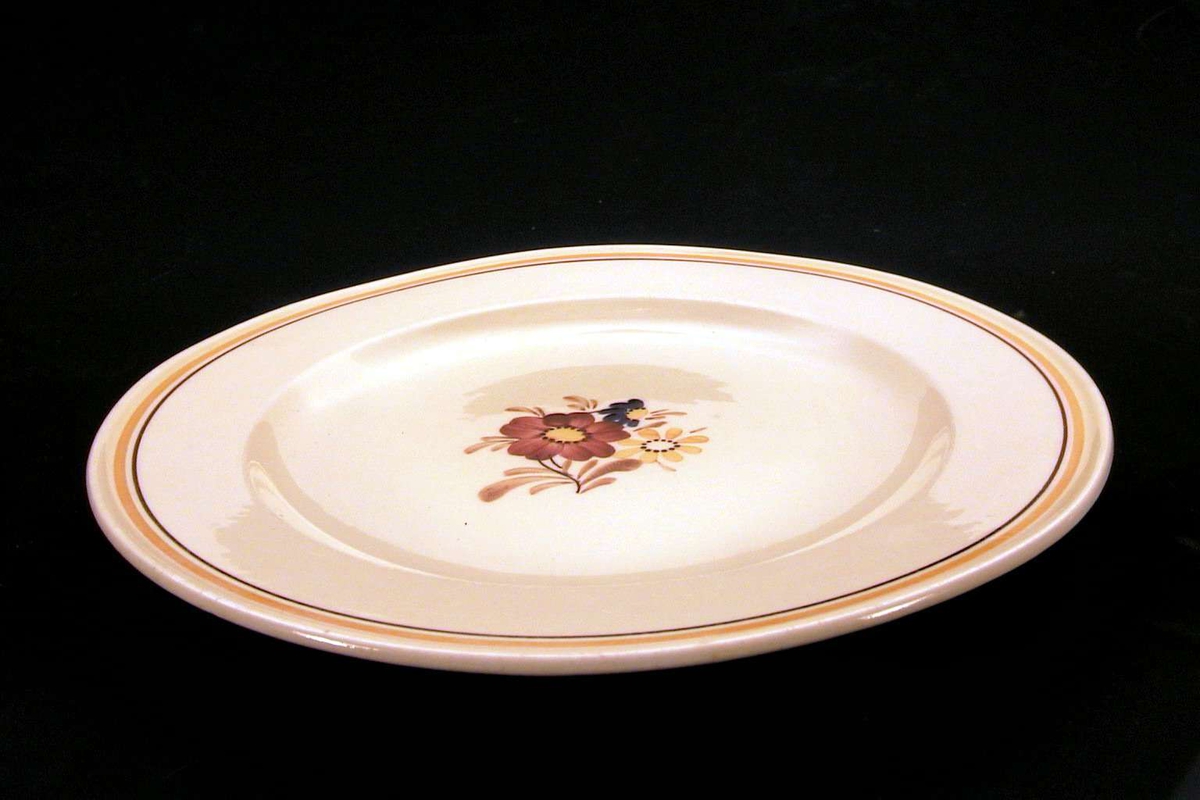 Gul tallerken med blomsterdekor på midten, langs kanten en oker og en brun linje. 