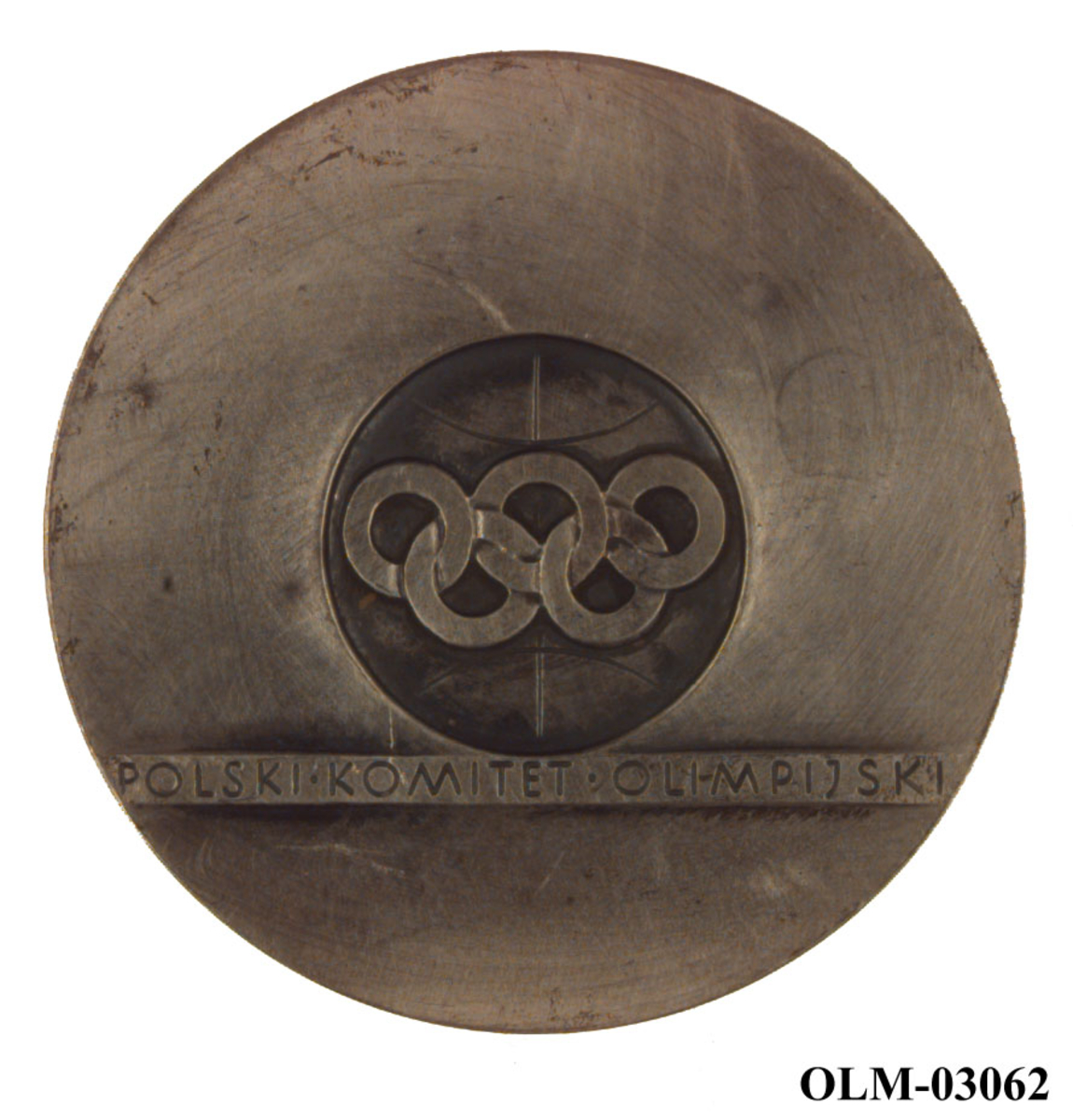 Sølvfarget medalje med motiv av de olympiske ringer og løpende atleter. Det er også et stilisert mønster/motiv på medaljen. Det følger med en rød eske til medaljen.