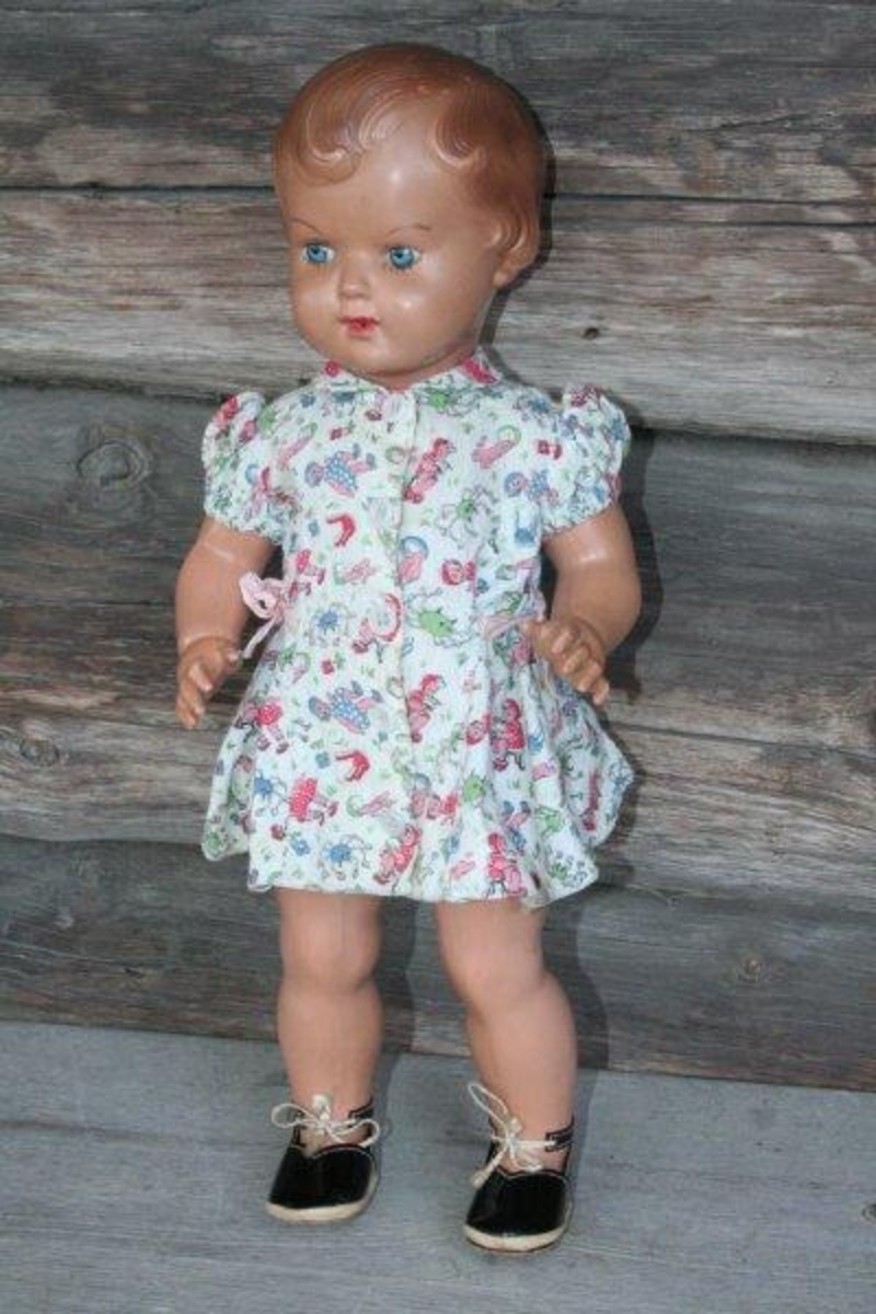 Hele dukken er støpt i celluloid. Påmalte blå øyne, brune øyenbryn, rød munn. Støpt, brunt hår. Kjolen er registrert som GH.07039.