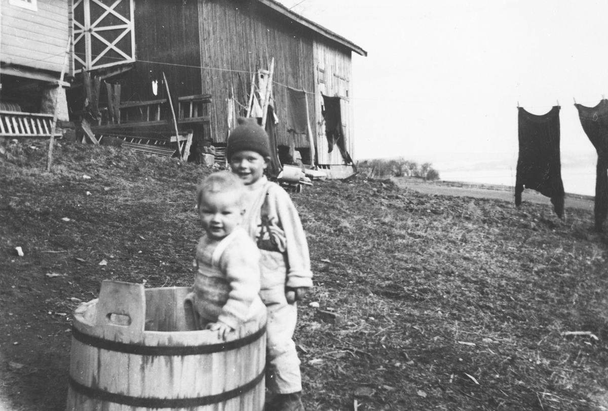 To små barn leker i saltebaljen på tunet. Klesvask til tørk på snor.