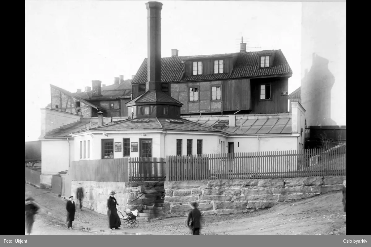 Fra gamle Enerhaugen. Enerhaugen bad en gang etter 1912. Tatt i bruk fra 1891. Lå bak Grønland kirke. Dame med barnevogn. Bygning med kull og koks bakenfor.