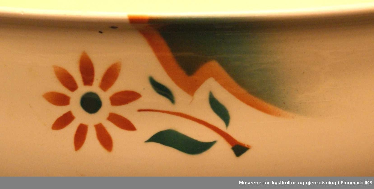 Tre identiske mønster er plassert på ytterkanten av vaskefatet. Motivet er en prestekrage-lignende blomst i orange og grønt som ligger vannrett bortover. Til høyre for blomsten går det et orange lyn, som nesten ser ut som det tegner en fjellside-profil. Til høyre for lynet er det et område farget grønt.