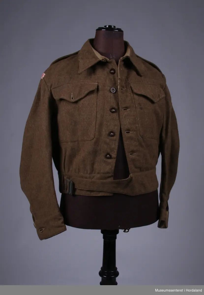 ...(20) Leeds 1943, 56003. Uniform består av 1 jakker, 1 skjorte, 1 bukse, 1 hue, 1 belte, 1 par gamasjer, 1 slips og 1 epålett. Jakka har påsydd Bjørn West stempel. På epåletten er det trykt på et norsk flagg og sydd på 3 raude striper.
