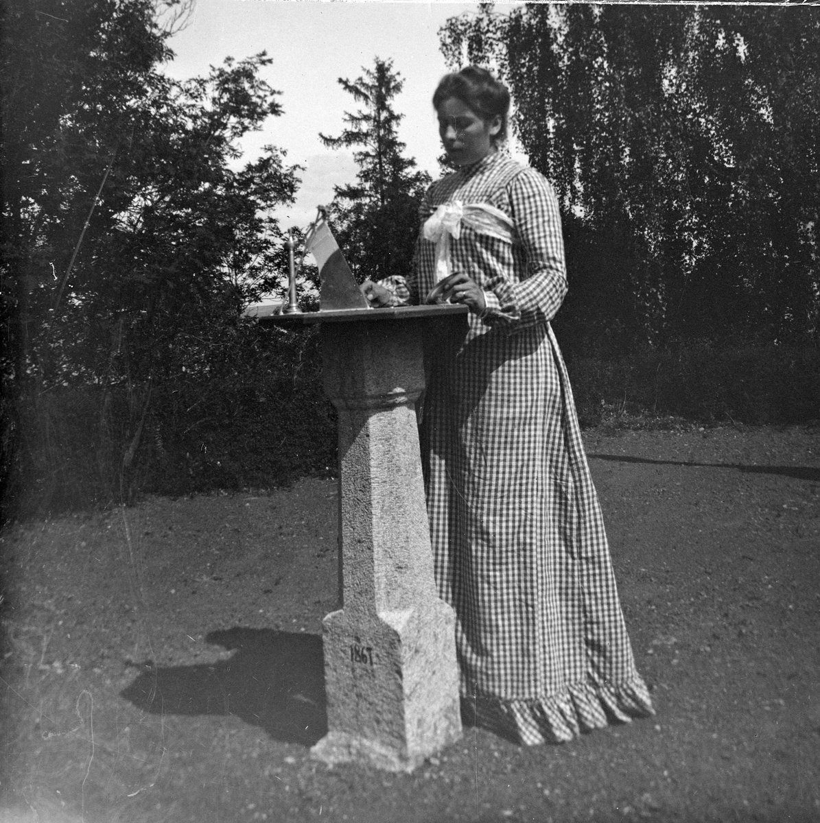 Anna Benjamine Hoel f.1872 står ved et solur, konstruert av Jacob Hoel. Hovinsholm gård, Helgøya i Ringsaker. Foto Jacob Hoel.