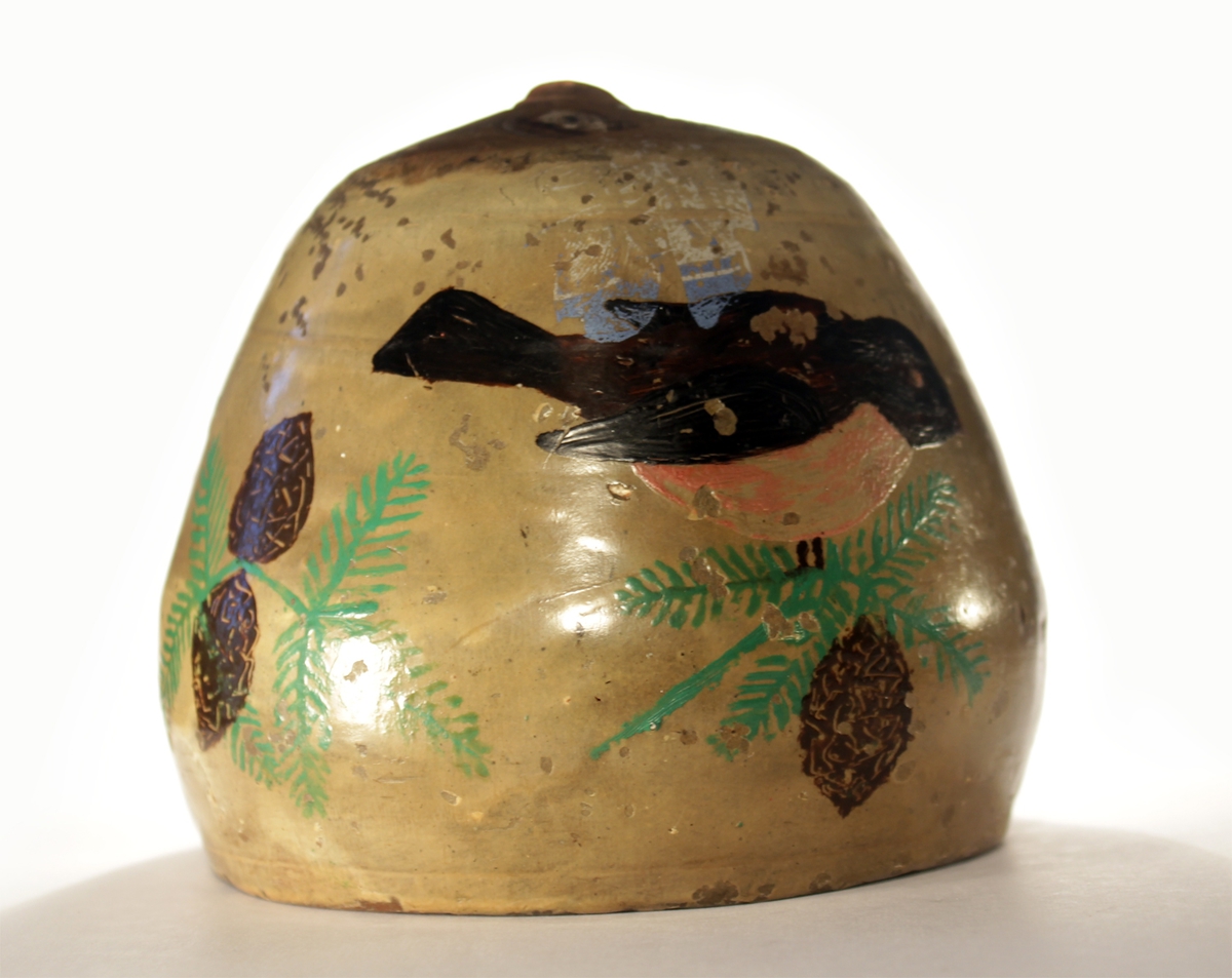 Sparebøssen er dekorert med granbar, kongler og en fugl. Et ansikt preger sparebøssen på oversiden. Munnen fungerer som åpning til å putte penger i.
