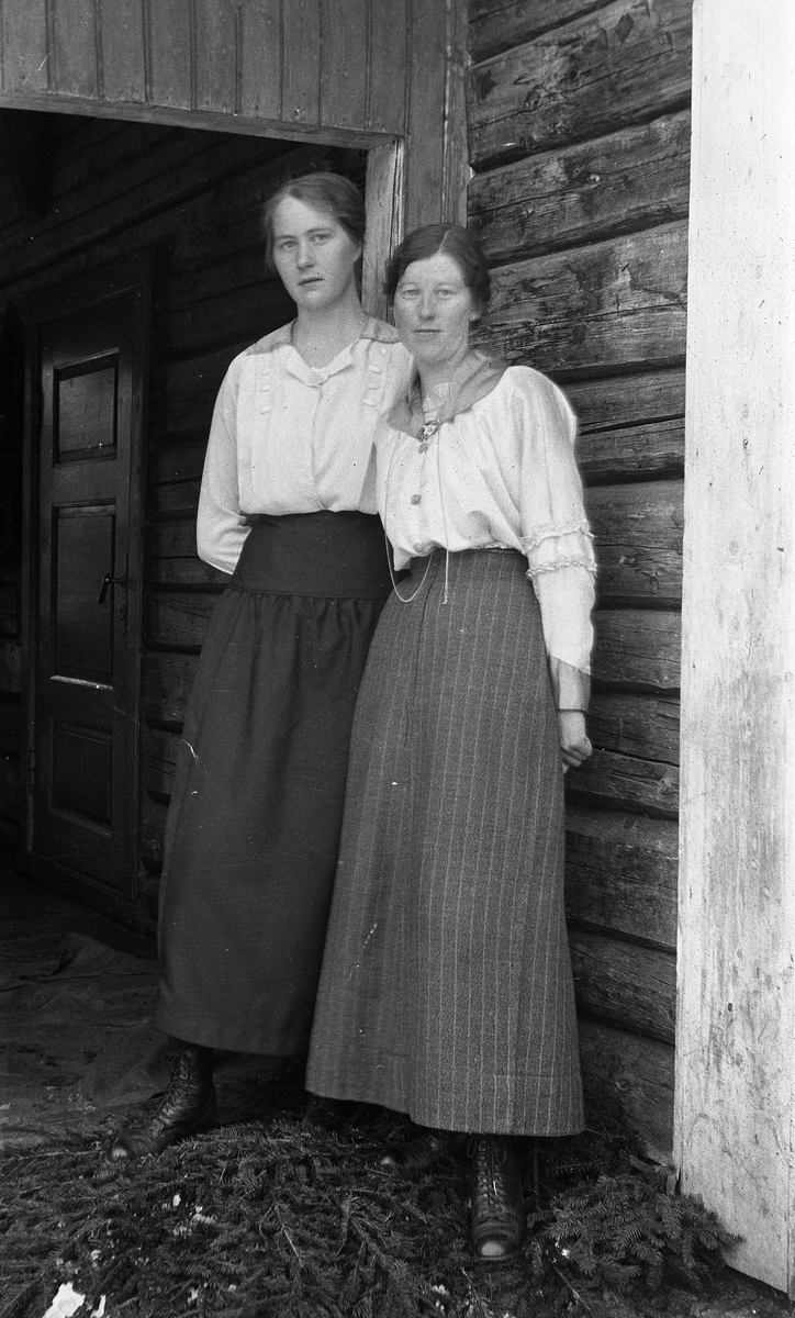 To kvinner i helfigur i en døråpning. Trolig på Krabysanden, Østre Toten. Kvinnene er ikke identifisert.