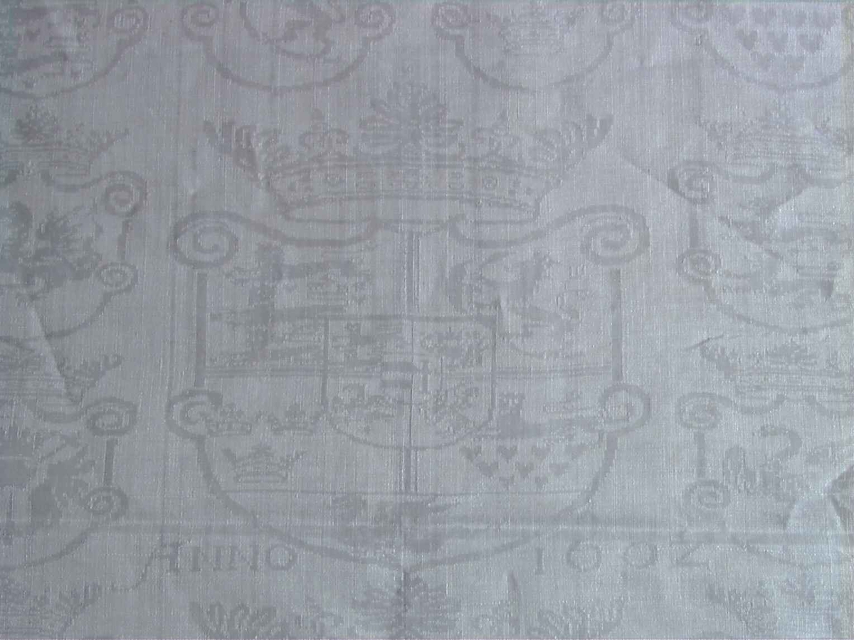 Det danske kongevåpen og Christian IV og Anna Catrines kronede navnetrakk omgitt av 16 skjold med alle de dansk-norske provinsers forskjellige våpenmerker. Dobbelt bord med våpentroféer, astronomiske instrumenter, jaktscener og fiskescener. Innvevd 1602 og brodert "H S II" i røde korssting.