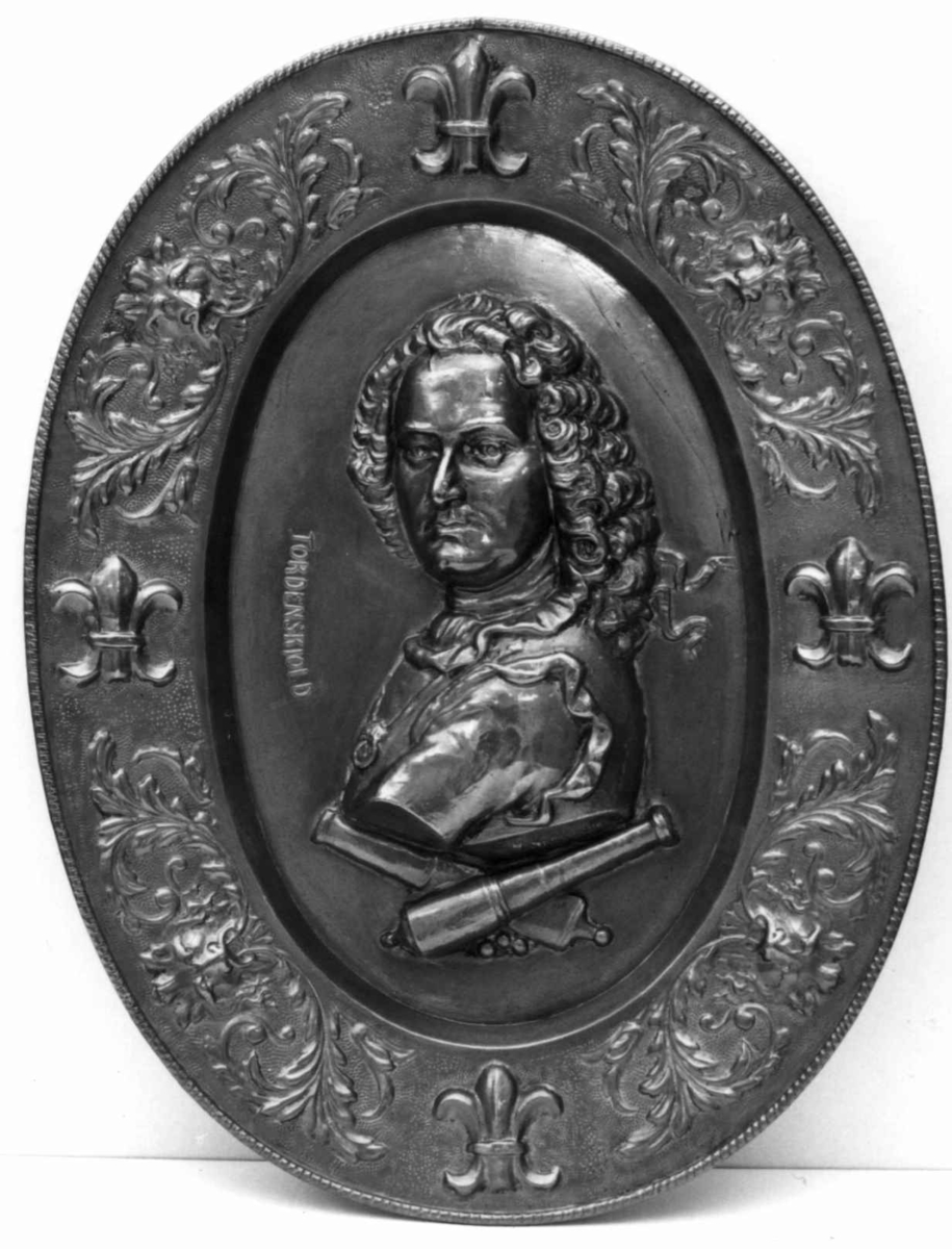 Messing. Ovalt, i bunnen Tordenskjolds brystbilde i relieff, derunder 2 korslagte lavetter, border og franske liljer, akantus og løvemasker.