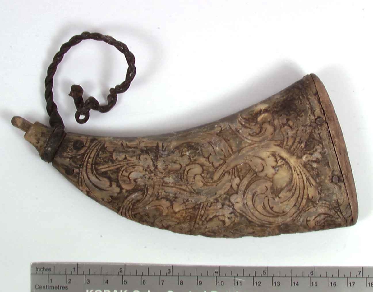 Flatt krutthorn av horn med rike utskjæringer av akantus, samt skinnsnor øverst og propp og bunn av tre.