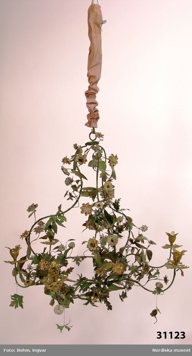 Ljuskrona, rokoko, så kallad lövverkskrona, av klippt och målad plåt. Utformad som ett naturalistiskt lövverk med gröna blad och flerfärgade blommor på en päronformad stomme. Sex svängda ljusarmar med blomkalksformade ljuspipor av förgylld mässing. Kedja för upphängning.
Anm: Kronan konserverades 2013.
/Anna Womack 2015-06-05