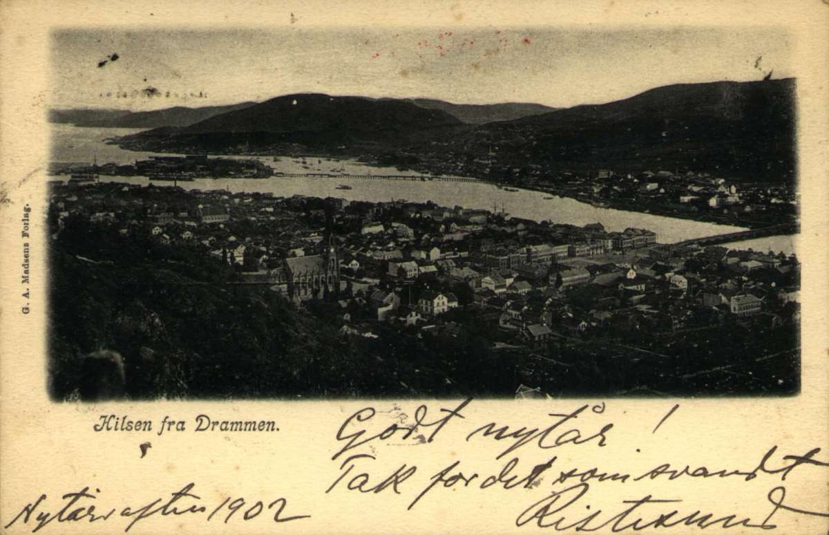Postkort, Nyttårshilsen. Fotografisk motiv. Svart/hvitt. Oversiktsbilde over Strømsø bydel i Drammen. Bybebyggelse med elva og broer.  I bakgrunnen ses Bragernes bydel omgitt av åser.