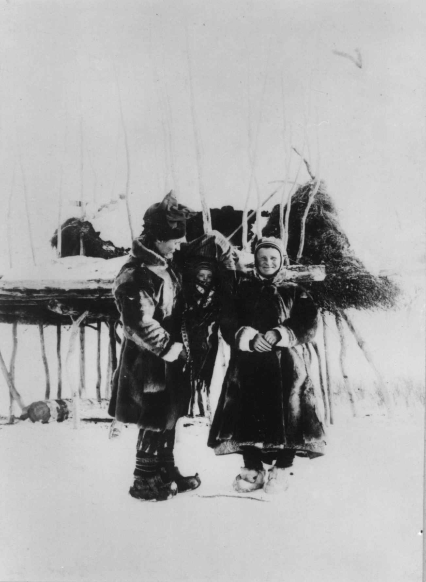 Mann og kvinne med et barn i komse, Ole og Marit Banne med datteren Inga,ved stillas?, Sør-Varanger, Finnmark, ca. 1900.