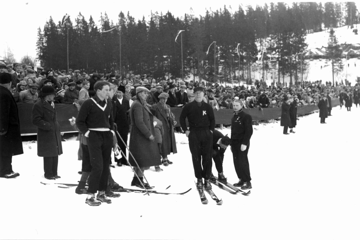 Ski. Hopprenn. Holmenkollen, Oslo 1934. Hoppere og funksjonærer står på sletta. Publikum i bakgrunnen.