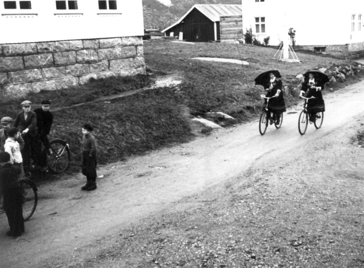 Valle, Aust-Agder 1938. Bededag. folk med sykler og parapyer på vei til kirken en regværsdag. Bygninger langs veien.