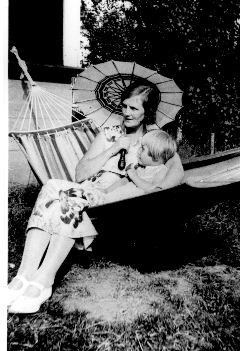 Mor og datter i hengekøye i hage. Astrid og Jorunn Fossberg i  sommerhuset de leide på Nærsnes i Røyken, Buskerud somrene 1929-36.  
Fra Jorunn Fossbergs private fotoalbum.
