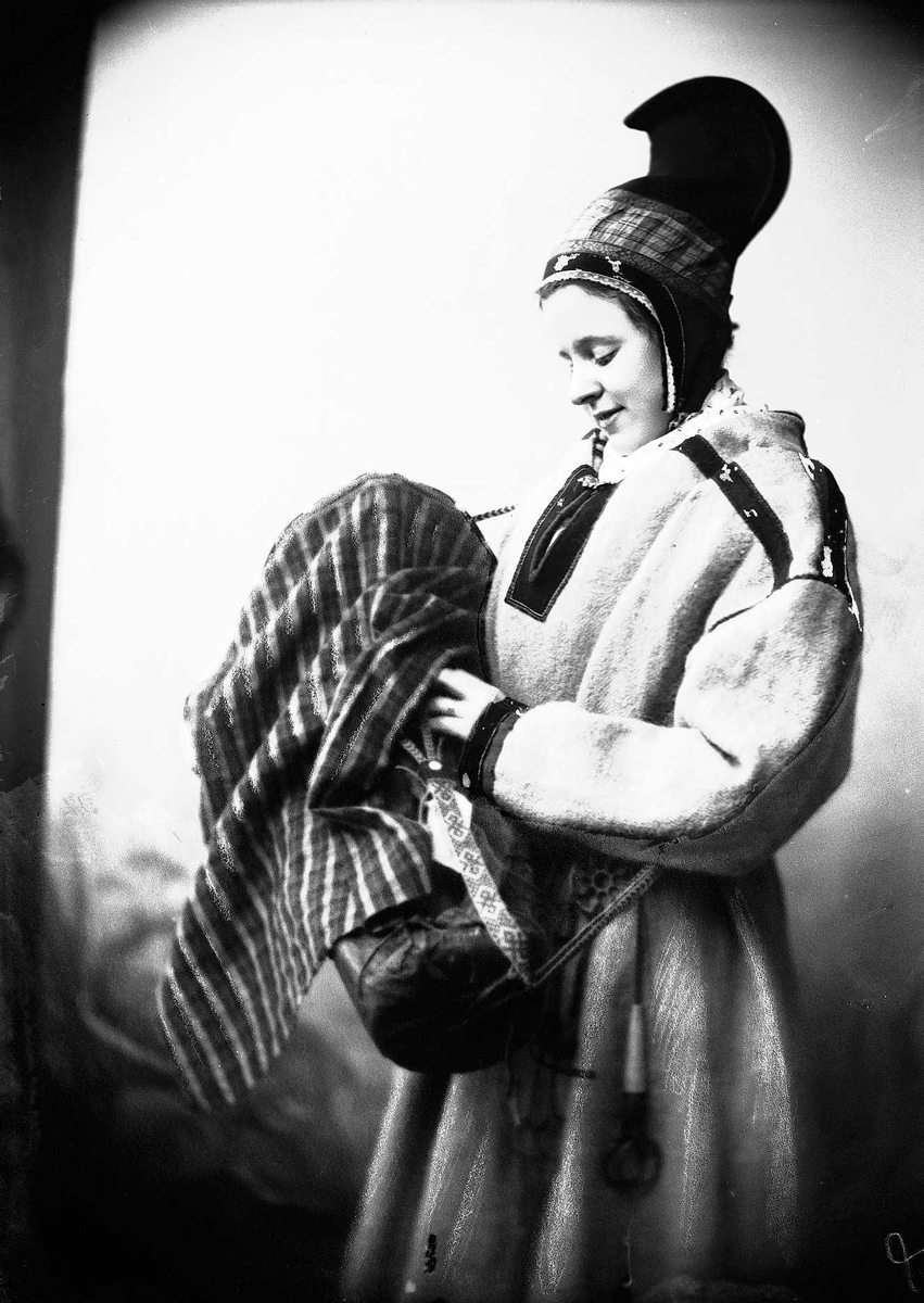 Kvinne ikledd samiske klær: kofte, belte, hornlue og komse. Beltering med nålehus.